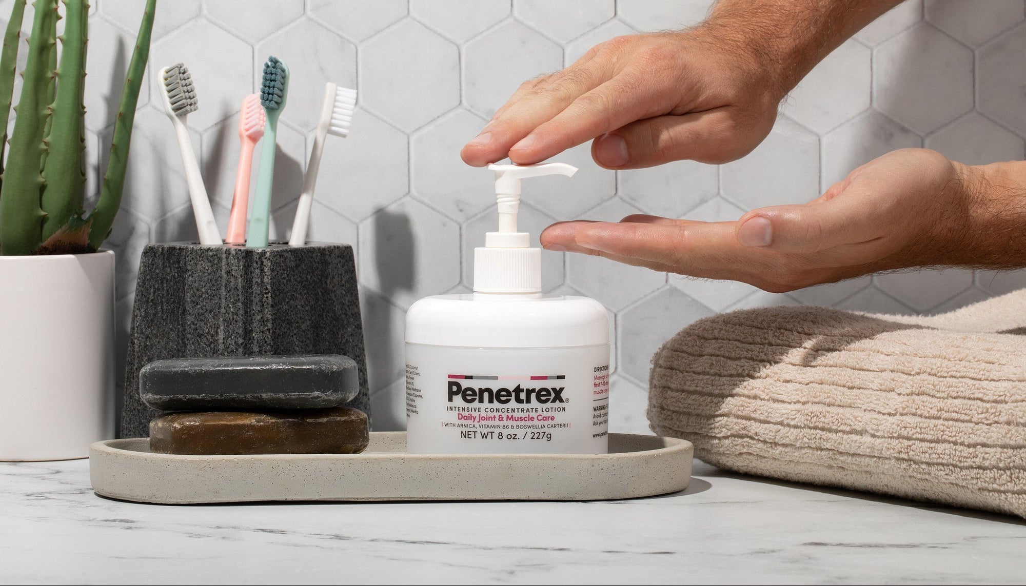 Person applying Penetrex cream from a pump bottle on a bathroom counter with toothbrushes and a plant in the background.